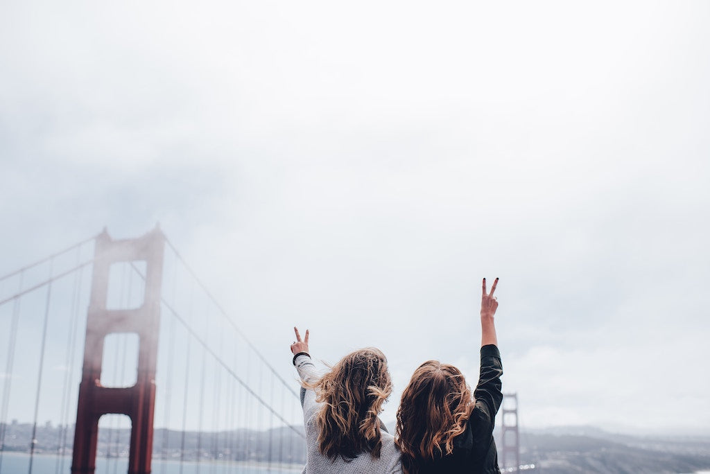 Two girls traveling together and giving the "peace sign" to the Golden Gate Bridge.